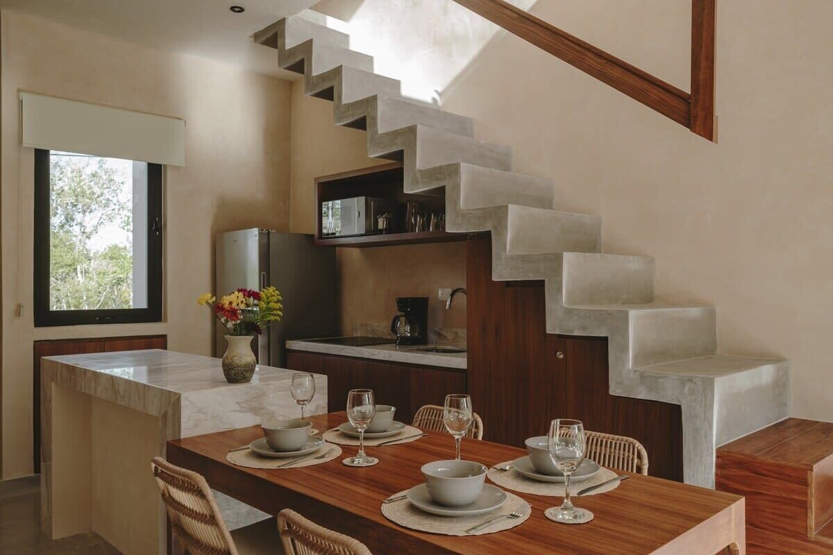 A modern kitchen with a marble countertop, a dining area with a wooden table set for four, and a unique staircase with a concrete finish.
