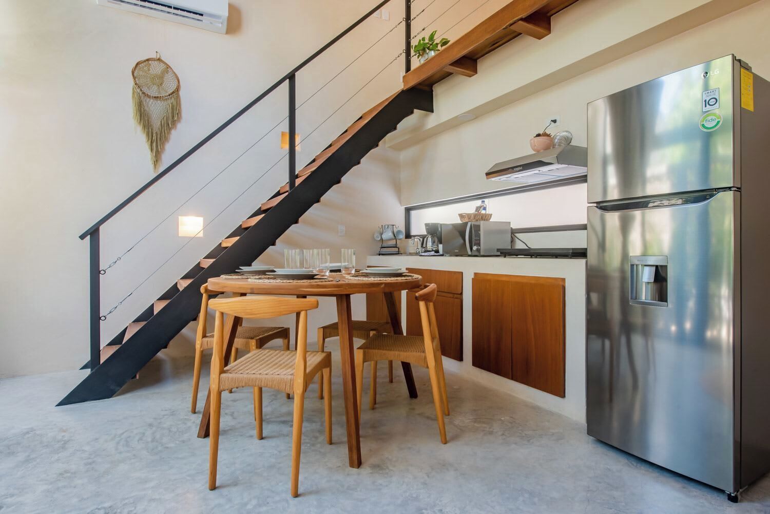 A modern kitchen with a stainless steel refrigerator, wooden dining table, and a staircase with black railings.