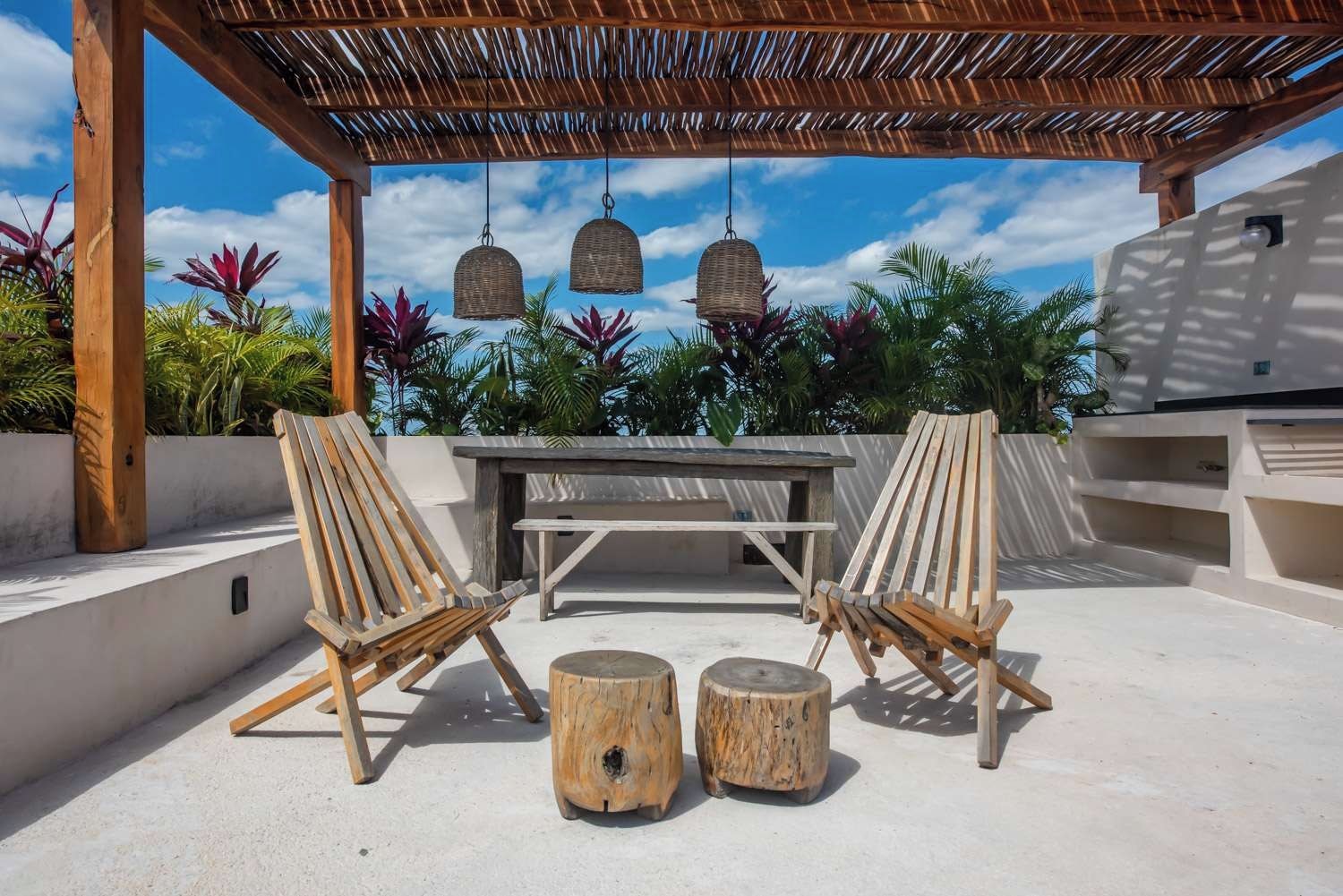 An outdoor patio with two wooden chairs, a table, and hanging wicker lamps.