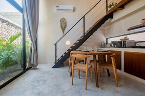 A modern kitchen with a dining area, a staircase, and a large window overlooking greenery.