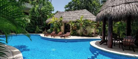 A swimming pool with a tropical setting, including palm trees and thatched-roof structures.