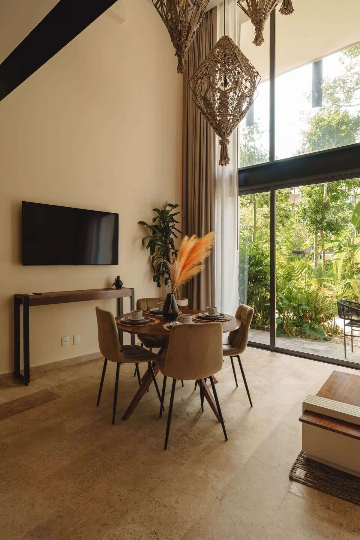 A modern dining area with a large window, a flat-screen TV, and a decorative hanging light fixture.