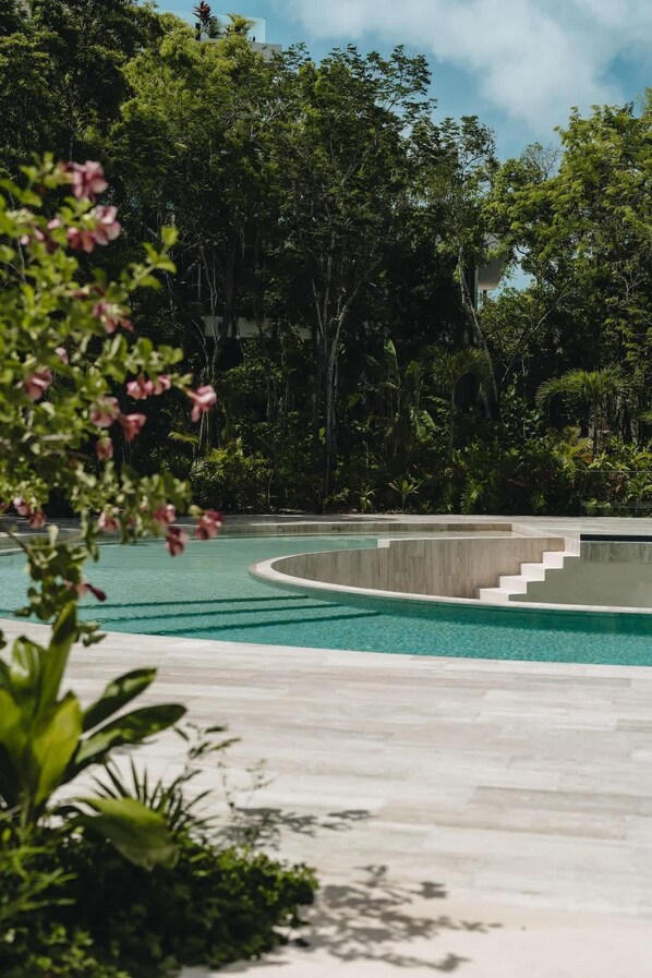 Una piscina moderna con design sinuoso, immersa nel verde e sotto un cielo limpido.
