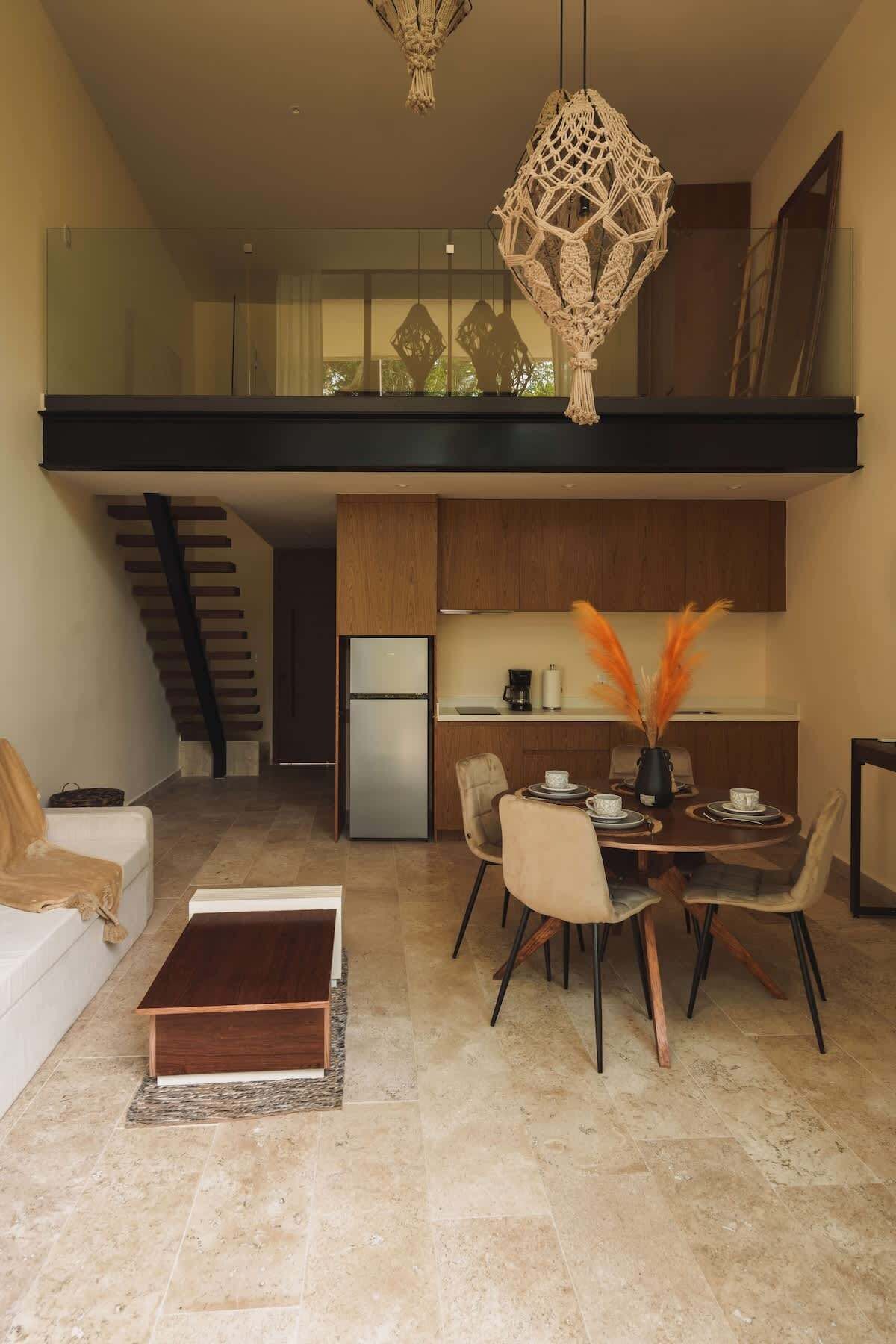 Een moderne keuken met een eethoek, een trap naar een hoger niveau, en een decoratief macramé kunstwerk boven de tafel.