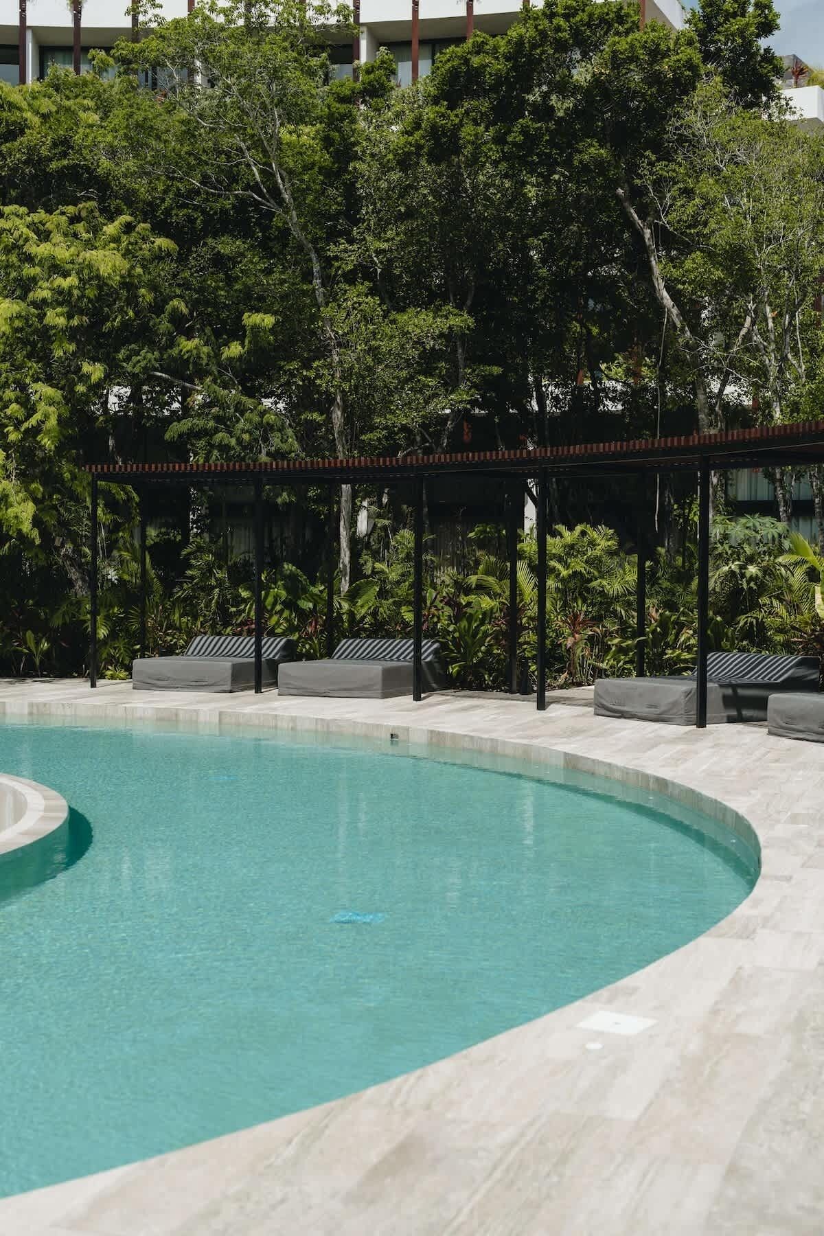 A swimming pool with a curved edge, surrounded by a covered seating area with benches.