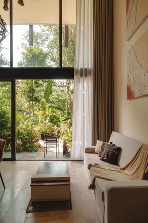 A modern living room with a large glass door leading to a lush garden. - Luxury Loft w/ Pools, Gym, Rooftop Panoramic Views (Tulum)