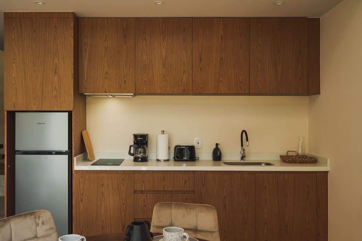 Eine kleine Küche mit Holzausstattung, einem Kühlschrank, einer Kaffeemaschine, einem Toaster und einem Spülbecken.