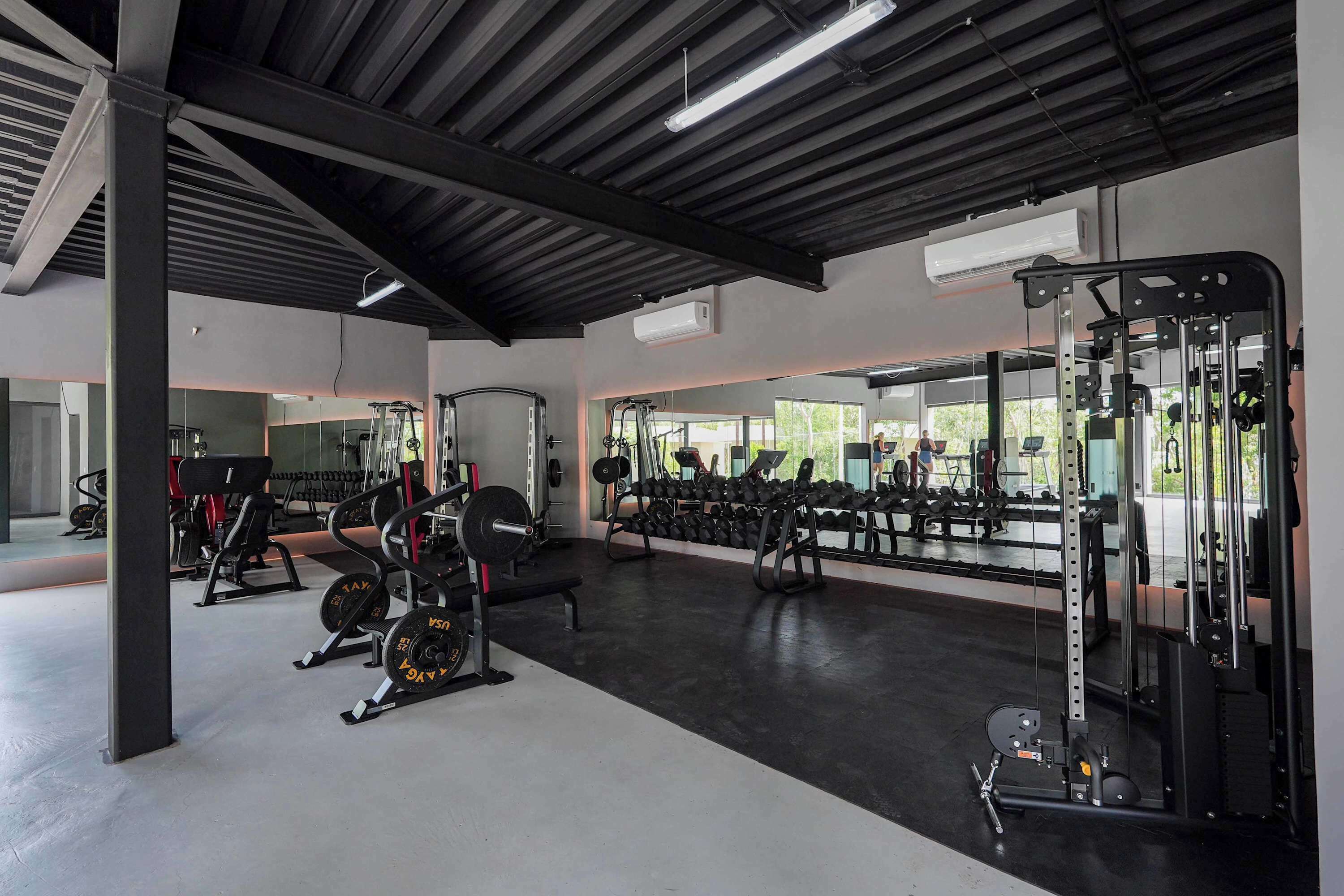 A gym with weightlifting equipment, mirrors, and a large window.