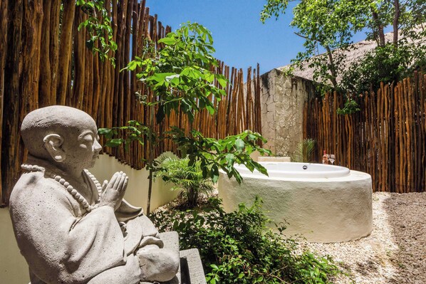 A statue in a garden with a stone wall and a hot tub.