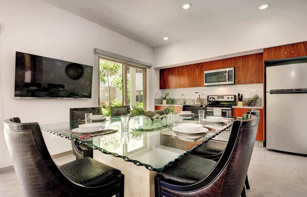 A modern kitchen with a glass dining table, wooden cabinets, and stainless steel appliances.
