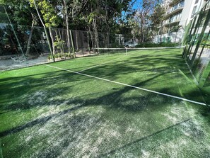 A tennis court with a net, surrounded by a fence and trees.