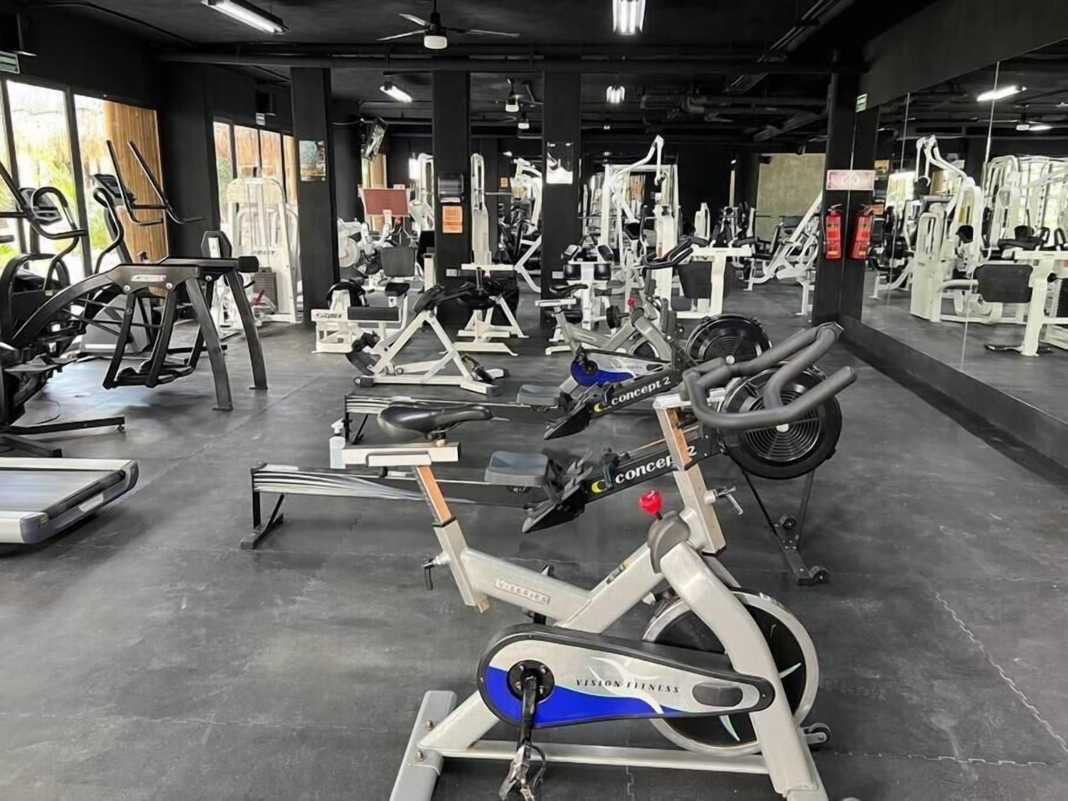 Un gimnasio con diverso equipo de ejercicio, incluyendo cintas de correr, bicicletas estáticas y máquinas de pesas.
