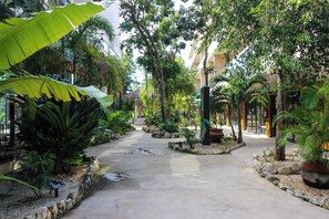 A pathway flanked by tropical plants and a building with a covered walkway. - Luxury Studio w/ Rooftop Pool, Padel Court & Gym (Tulum)