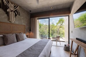 A modern bedroom with a large bed, a wooden headboard, a TV, and a balcony with a view of trees.
