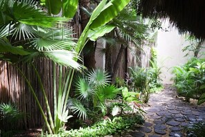 A garden pathway with tropical plants and a thatched roof structure.