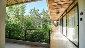 A balcony with a view of greenery, a wooden ceiling, and a glass door. - Tulum Penthouse with Rooftop Pool and BBQ Grill (Tulum)
