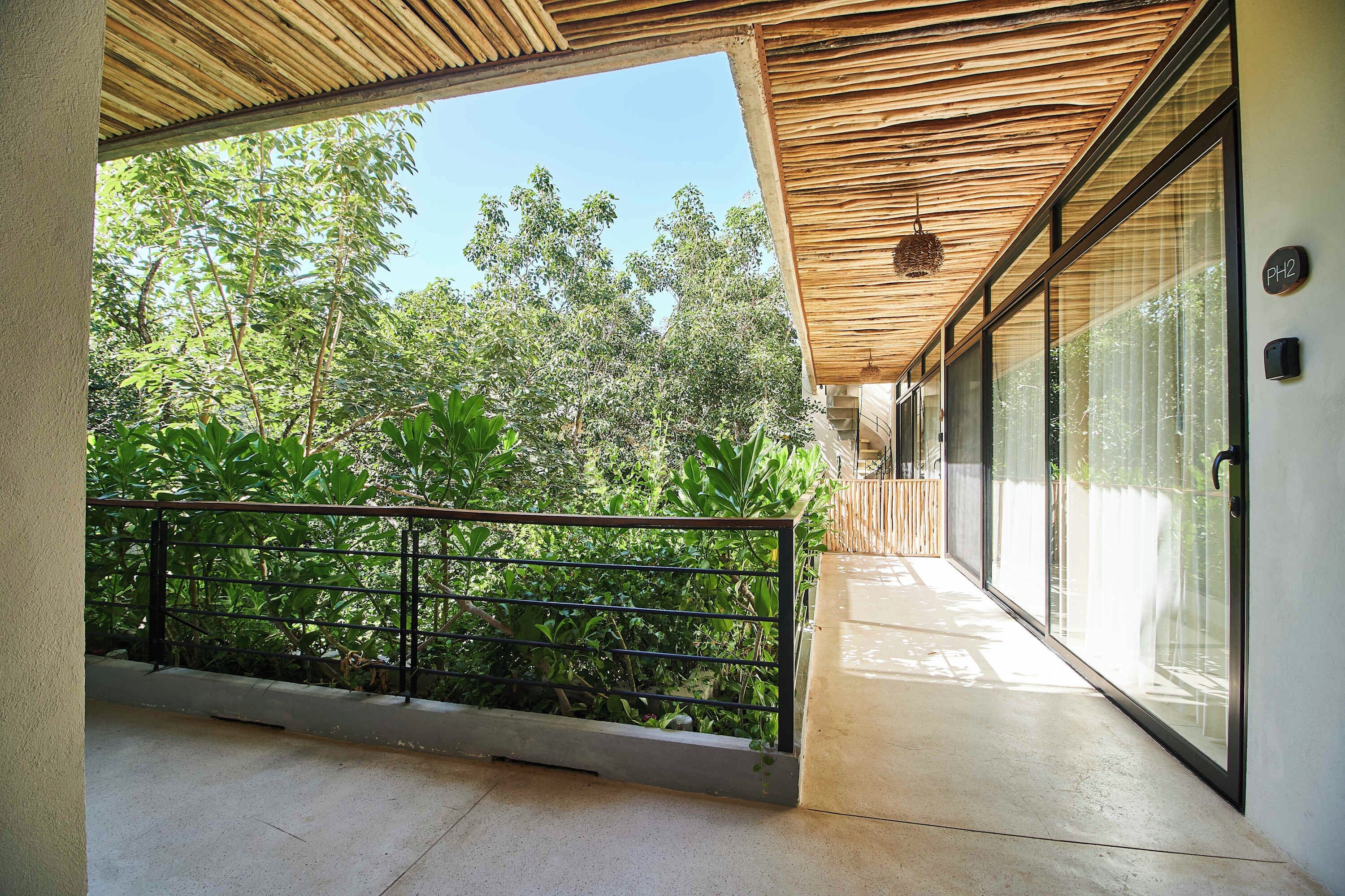 Ein Balkon mit Holzboden, Glastüren und Blick auf üppiges Grün.