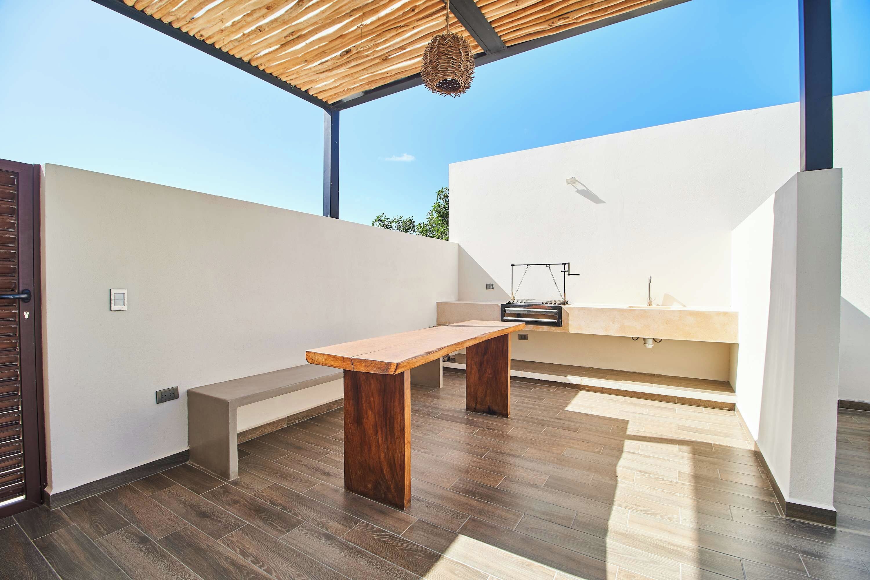 Un área de cocina exterior moderna con una mesa de madera y una parrilla de barbacoa integrada.