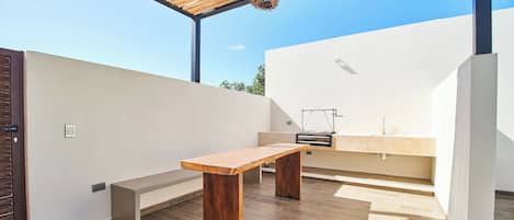 Un área de cocina exterior moderna con una mesa de madera y una parrilla de barbacoa integrada.