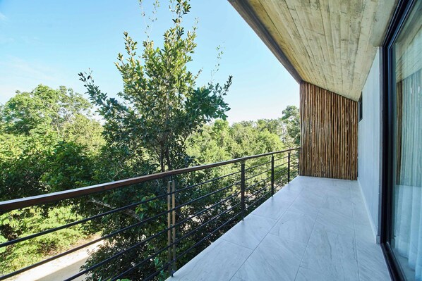 A balcony with a view of a lush green landscape, a metal railing, and a concrete structure. - Tulum Penthouse with Rooftop Pool and BBQ Grill (Tulum)