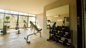 A gym with exercise equipment, a mirror, and a window with a view of outdoor exercise bikes. - Tulum Penthouse with Rooftop Pool and BBQ Grill (Tulum)