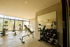 A gym with exercise equipment, a mirror, and a window with a view of outdoor exercise bikes.