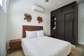 A bedroom with a bed, nightstand, wall-mounted air conditioner, decorative wall art, and a dark wardrobe.
