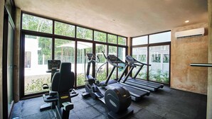 Ett gym med löpband, en motionscykel och styrketräningsmaskiner, stora fönster med utsikt över grönområden.