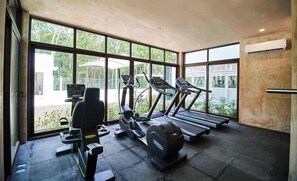 A gym with treadmills, a stationary bike, and weight machines, large windows with a view of greenery.