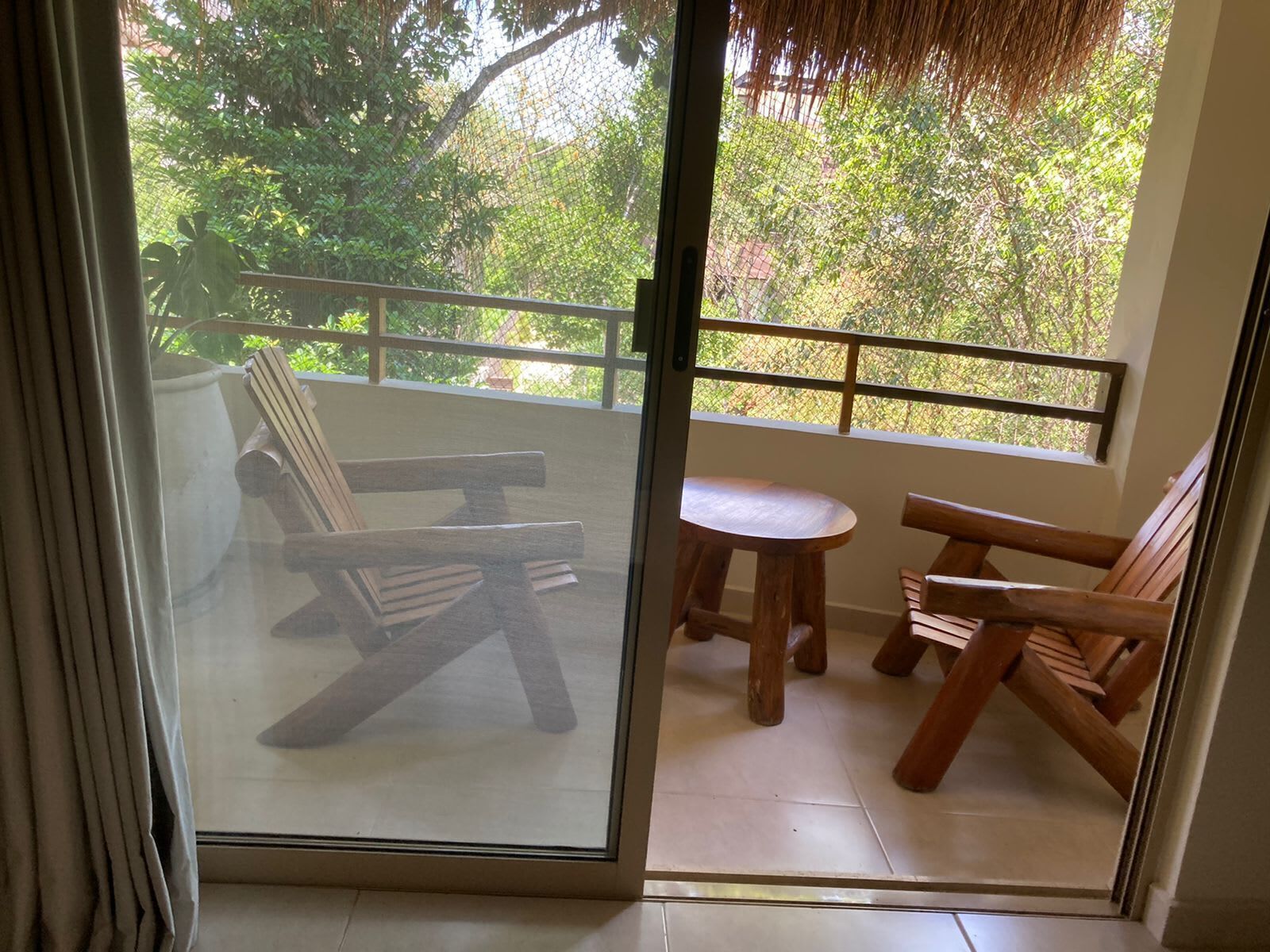 A balcony with wooden furniture, including a table and chairs, and a view of greenery outside.