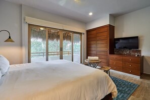 A bedroom with a large bed, a wooden wardrobe, a television, and a balcony with a view of greenery.