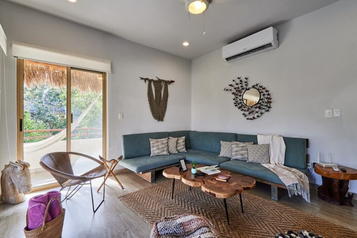A modern living room with a green sofa, a wooden coffee table, and a hammock by the window.