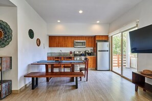 A modern kitchen with wooden cabinets, a dining table with benches, and a large window providing a view of the outdoors.