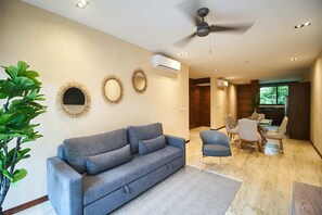Ein modernes Wohnzimmer mit grauem Sofa, Esstisch, Stühlen und dekorativen Wandspiegeln.