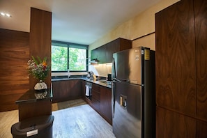 Cozinha moderna com armários de madeira escura, geladeira de aço inoxidável e janela com vista para o verde lá fora.