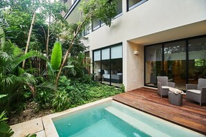 Una casa moderna con piscina, mobiliario exterior y abundante vegetación.