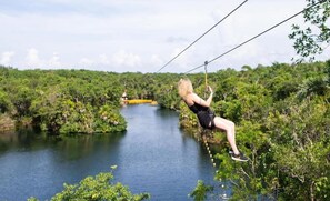 A person zip-lining over a river with dense greenery on both sides.