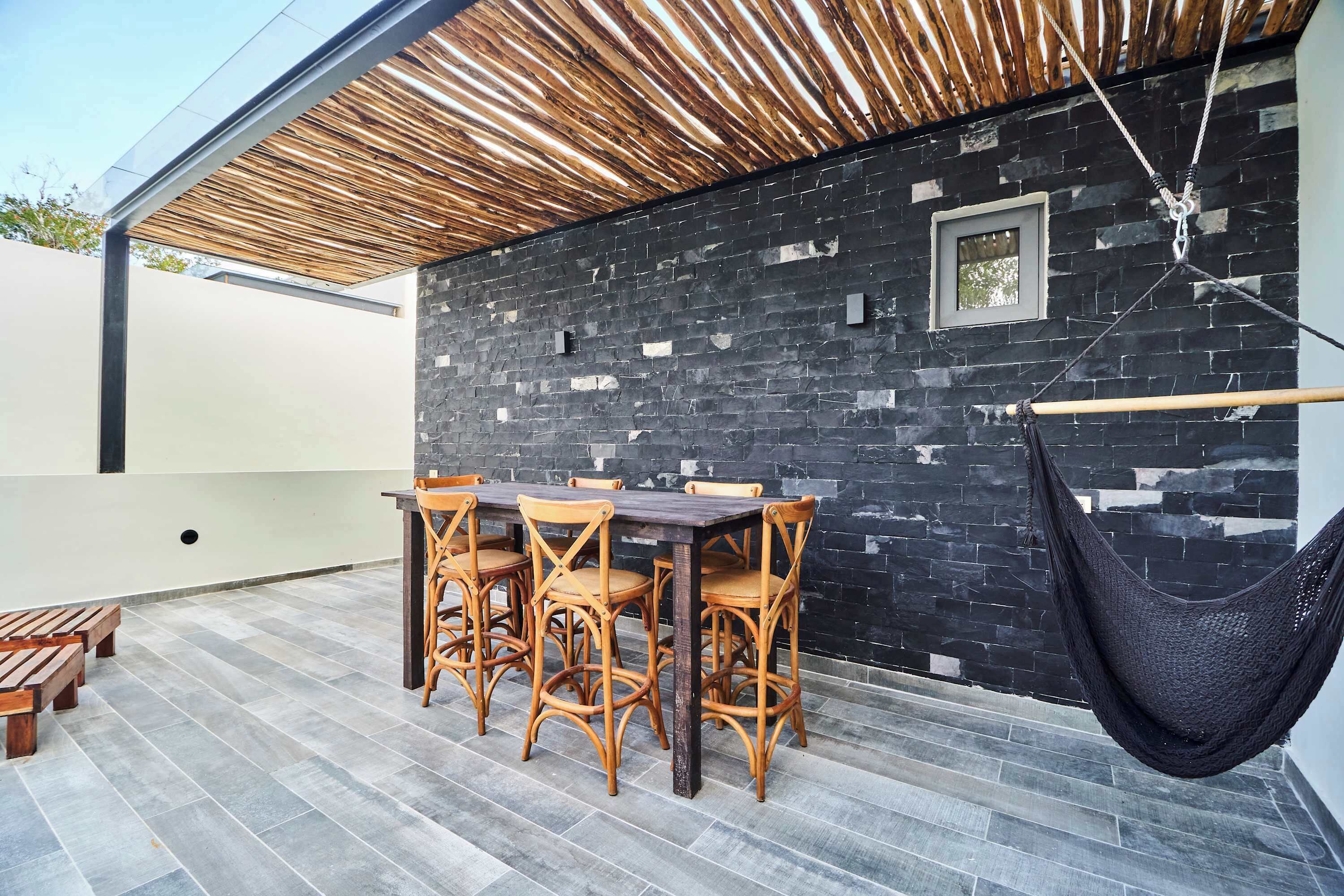 Un patio con una mesa y sillas, una hamaca y un muro de piedra.