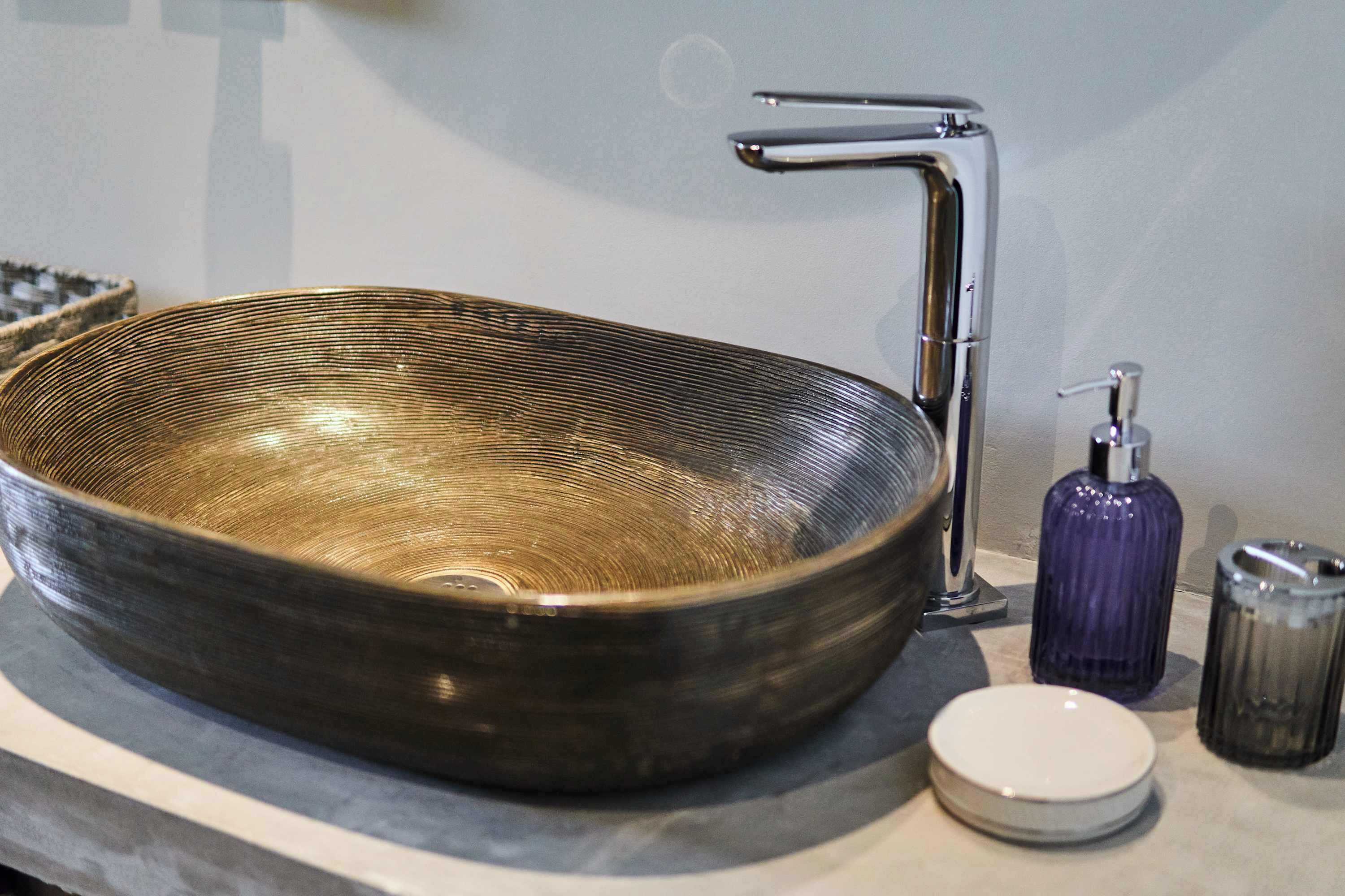 Une salle de bain dotée d’un grand lavabo de forme ovale, d’un robinet moderne, d’un distributeur de savon et d’un ensemble salière et poivrière.