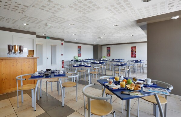 Cafetería con varias mesas y sillas, equipada con bandejas y distintos alimentos.