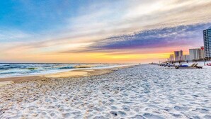 En strand med solnedgang, sandet bredde og bygninger i baggrunden.