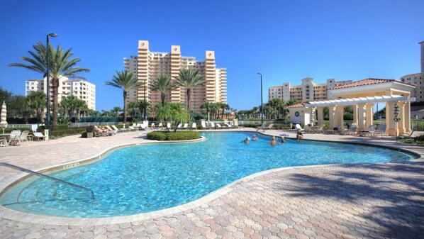 A swimming pool with a hexagonal tiled deck, surrounded by palm trees and lounge chairs.