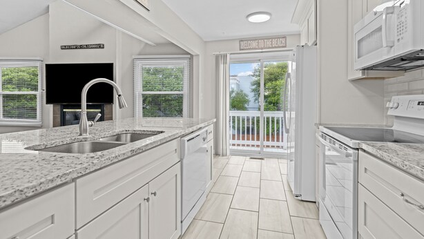 A modern kitchen with white cabinetry, granite countertops, a built-in oven, and a large window overlooking a balcony. - Cozy 3-bedroom condo with AC and WiFi in charming Virginia Beach (Virginia Beach)