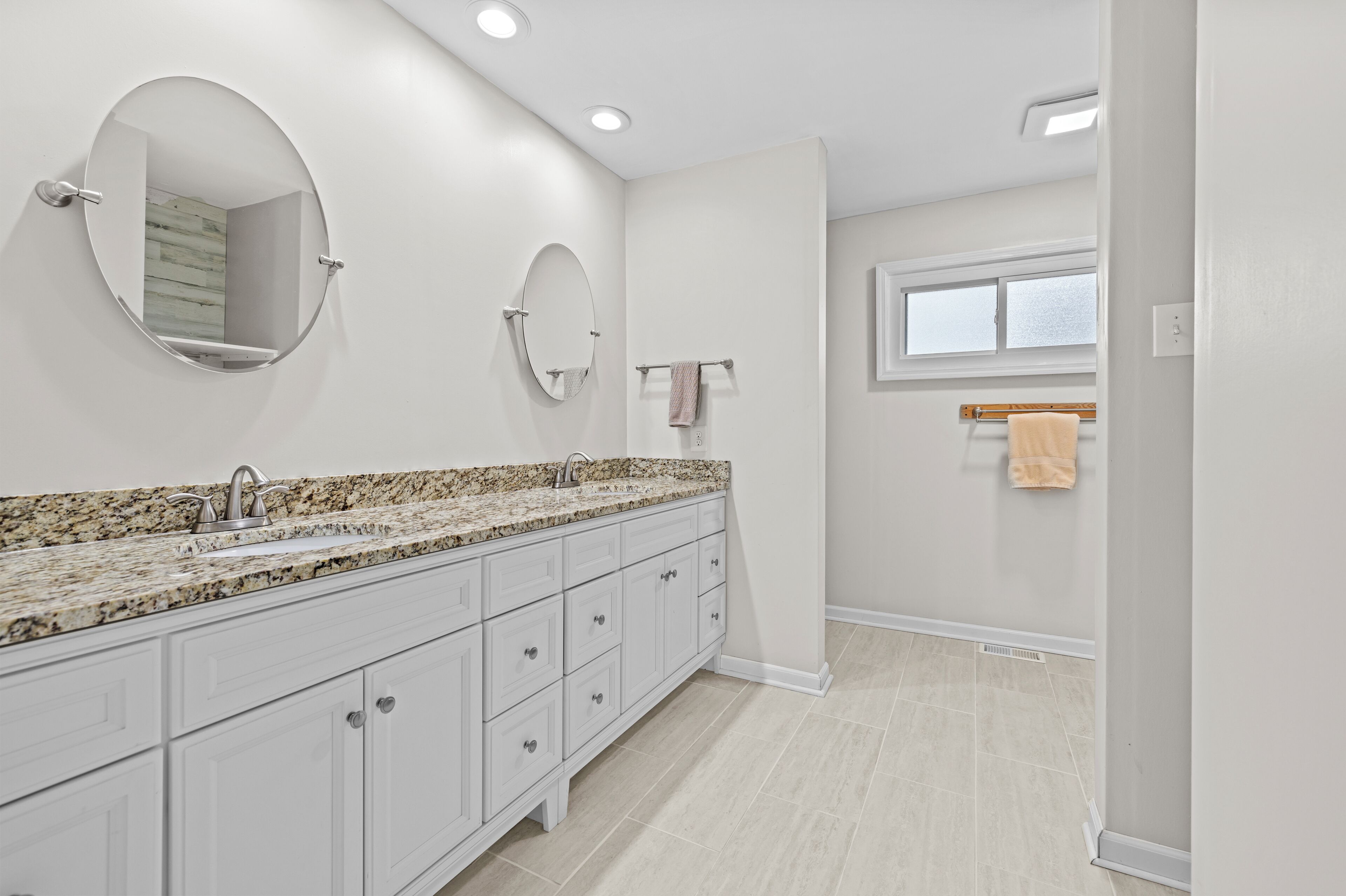 A modern bathroom with a granite countertop, two sinks, a large mirror, and a window.