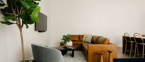 Una sala de estar moderna con un sofá marrón, un sillón gris, una mesita de centro y una planta en maceta.