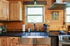 Una cocina con armarios de madera, un lavamanos de acero inoxidable, una estufa y un letrero de advertencia sobre no alimentar al Sasquatch.