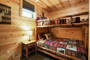 Una cabaña con literas, una pared de madera decorada con una cabeza de ciervo, una ventana con vistas y una lámpara en una mesita de noche.