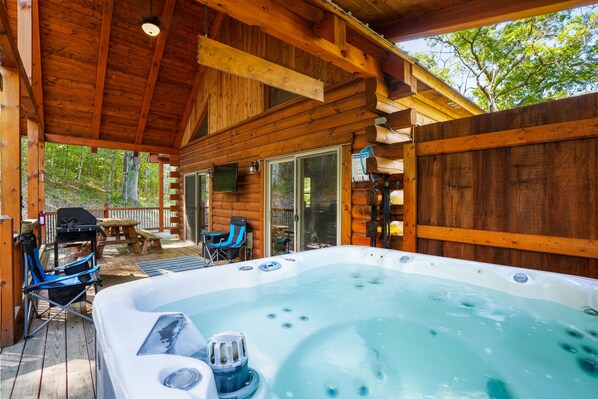 A wooden cabin with a hot tub, outdoor seating, and a grill area.