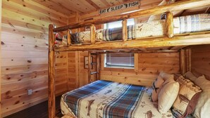 Et sommerhusinteriør med køjeseng, et vindue med rullegardiner og et skilt over sengen med teksten 'EAT SLEEP FISH'.
