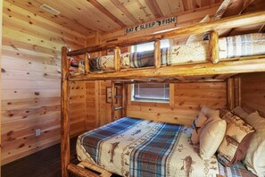 L’intérieur d’une cabine avec un lit superposé, une fenêtre avec des stores et une pancarte au-dessus du lit sur laquelle on peut lire : « MANGER, DORMIR, PÊCHER ».